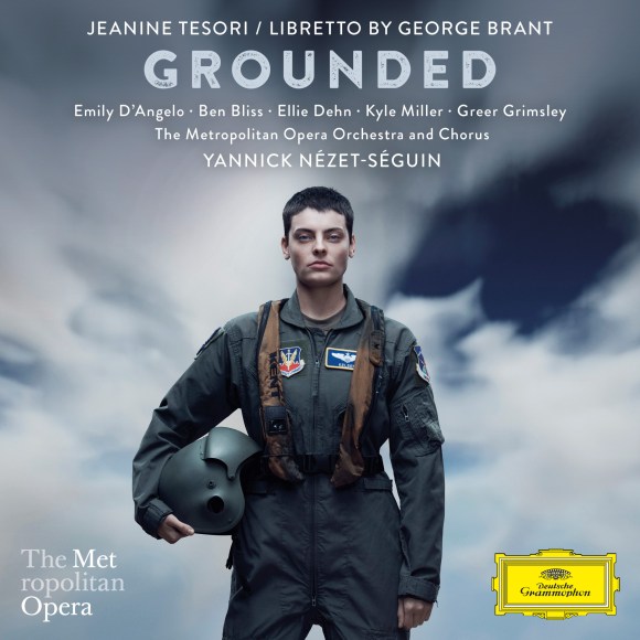 Poster for the opera Grounded: a short-haired woman in a military flight suit stands facing forward against a cloudy sky, holding a pilot’s helmet at her side. Text above reads “Jeanine Tesori / Libretto by George Brant” and the title “Grounded,” with cast names listed below. Additional text mentions the Metropolitan Opera Orchestra and Chorus conducted by Yannick Nézet-Séguin, with The Metropolitan Opera logo and the Deutsche Grammophon logo at the bottom.